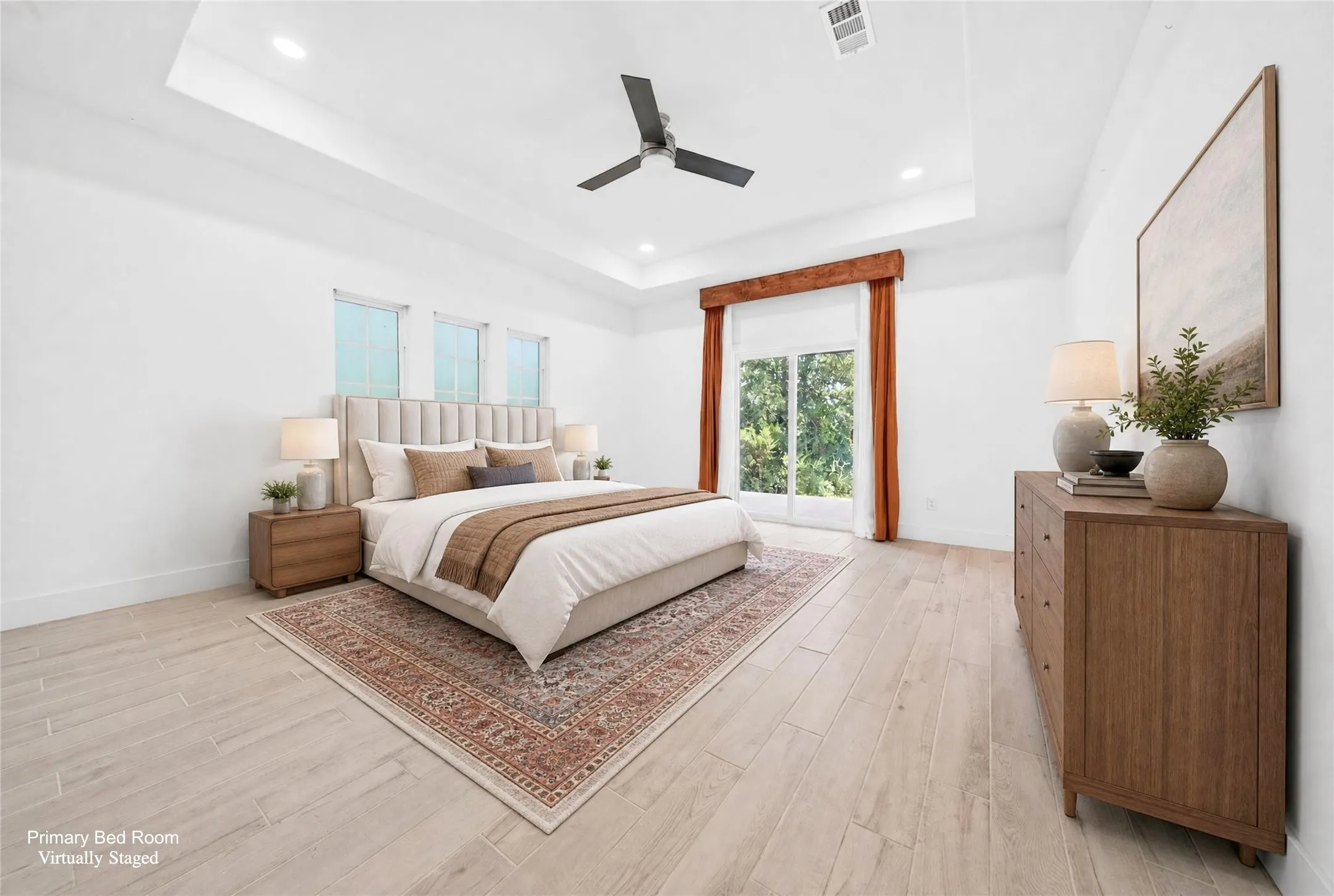 Spacious bedroom featuring light wood-finish flooring, a tray ceiling with recessed lighting and a ceiling fan, and a large glass door providing outdoor access