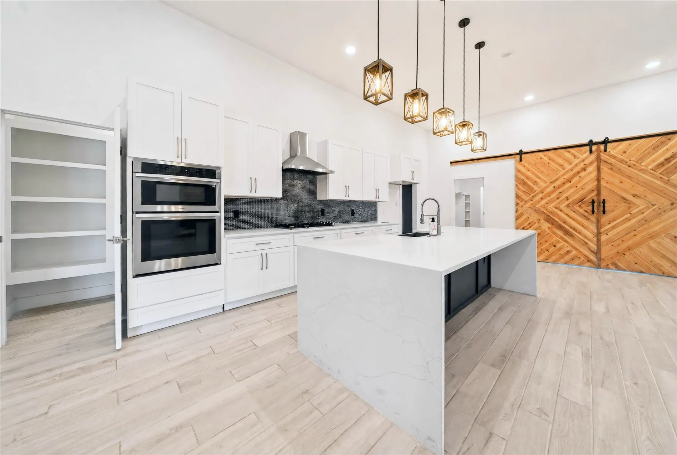 Modern kitchen featuring a waterfall island, stainless steel double oven, white shaker cabinetry, and a dark tile backsplash