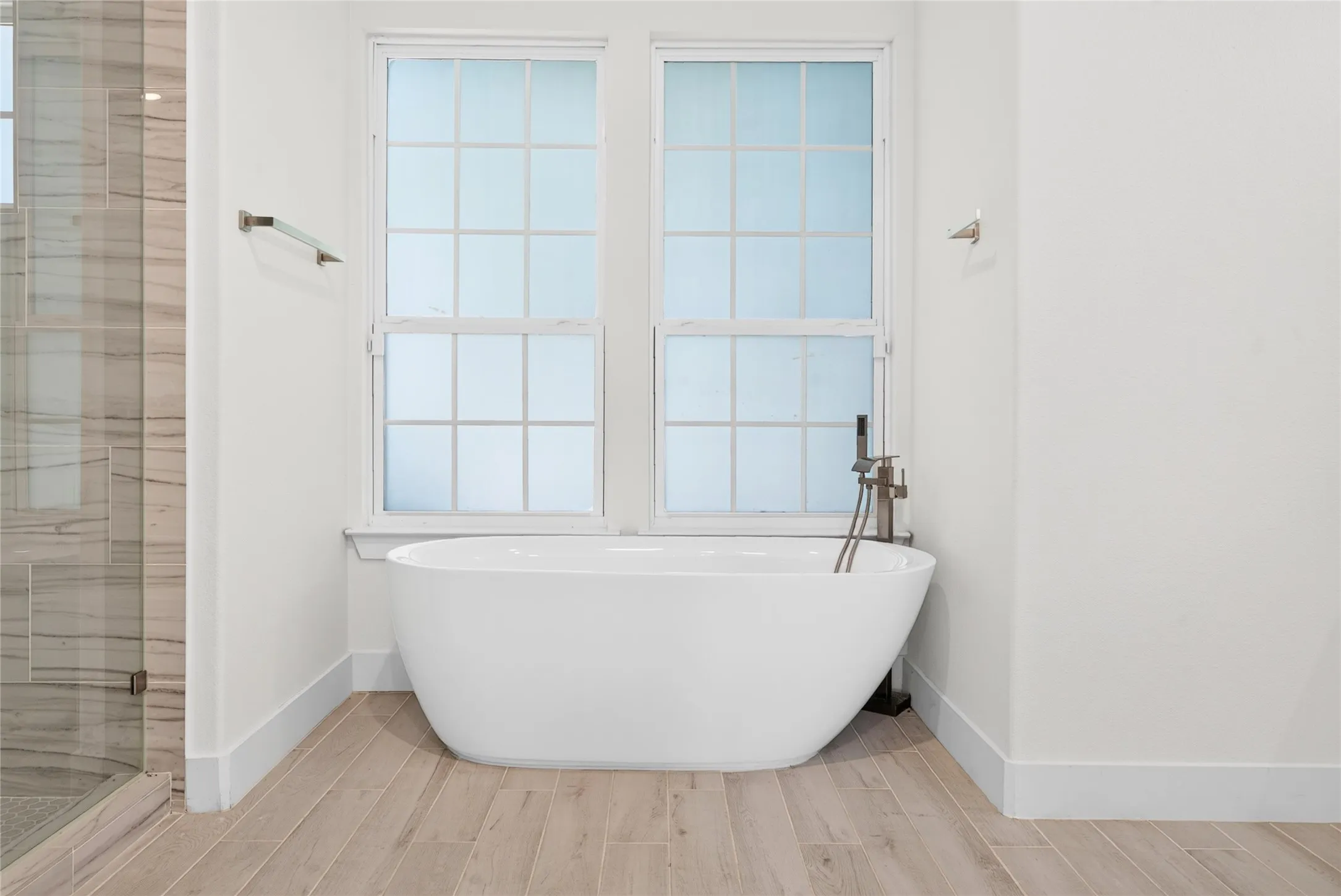 Freestanding soaking tub with floor-mounted faucet, set against two multi-pane windows