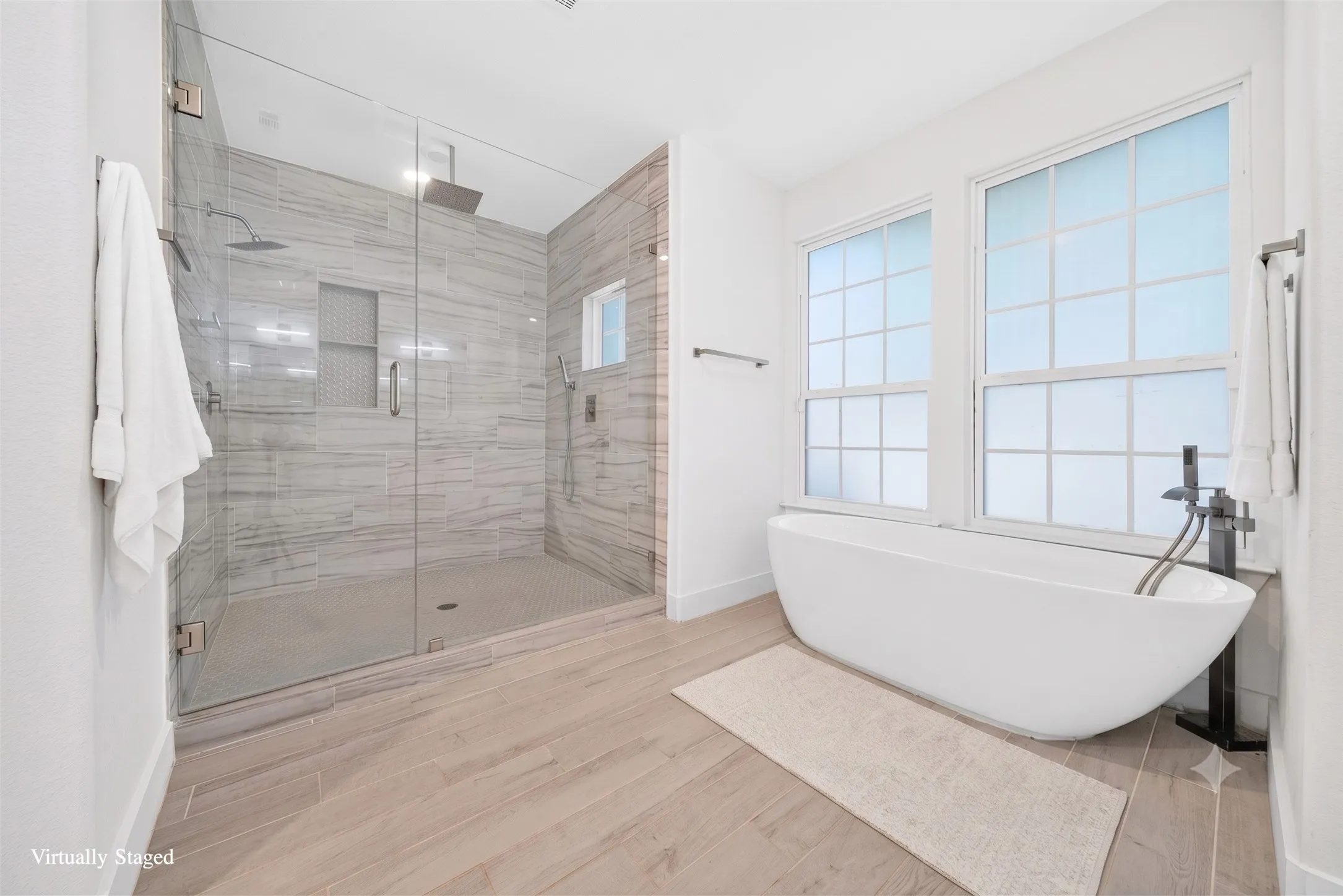 Bathroom featuring a spacious walk-in shower with glass enclosure, a freestanding soaking tub, wood-finish flooring, and two large windows