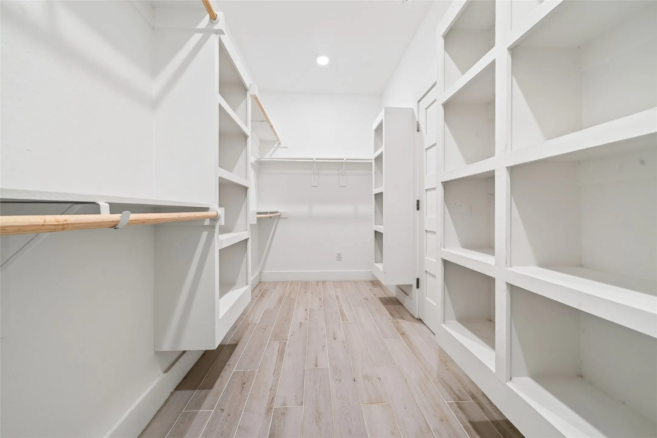 Spacious walk-in closet featuring extensive built-in shelving, hanging rods, and light wood-finish flooring