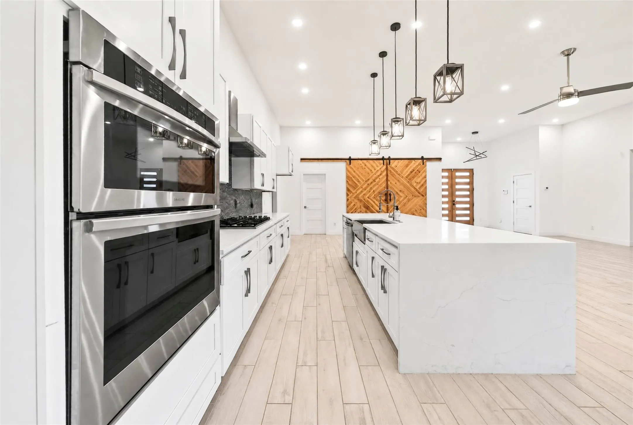 Modern kitchen featuring a waterfall island with an undermount sink, stainless steel appliances, white cabinetry, and wood-finish flooring