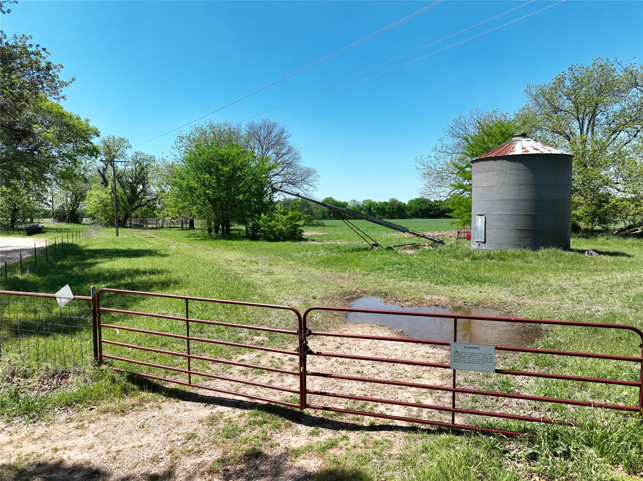 Expansive rural acreage featuring a large metal grain silo, an auger system, and a wide metal gate
