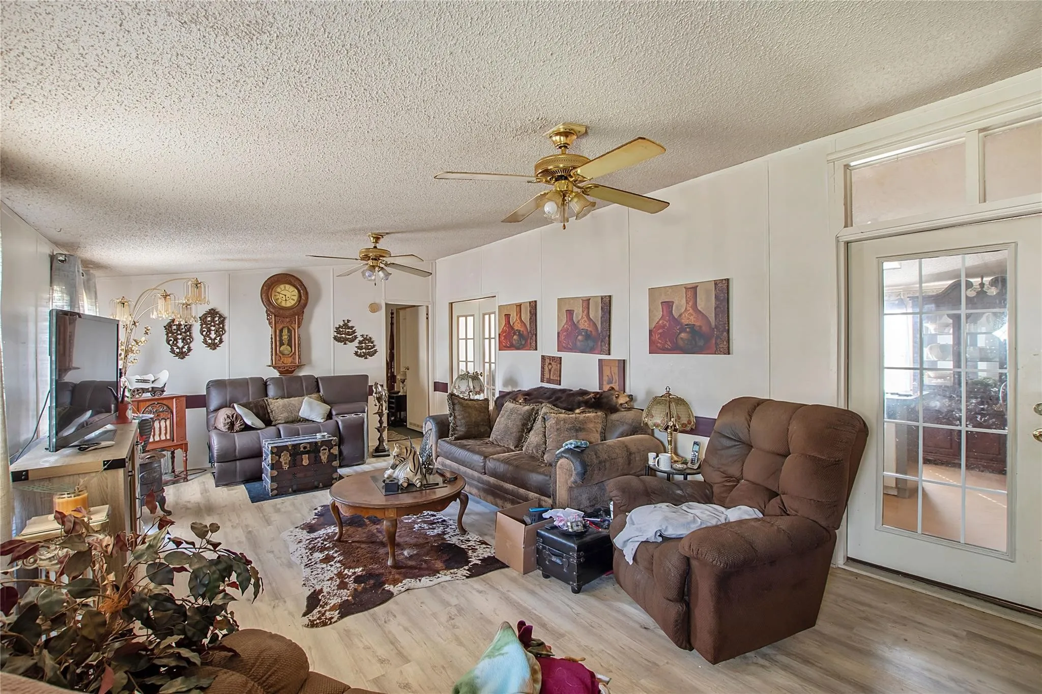 Spacious interior featuring wood-finish flooring, two ceiling fans with integrated lighting, and multiple windows with white trim