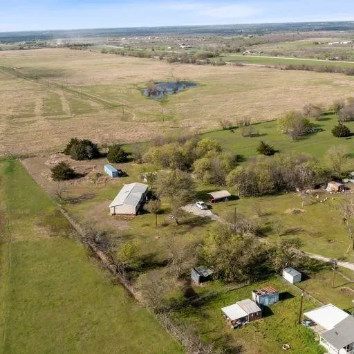 Expansive rural property featuring a large metal building, a distinct pond, varied mature trees, and open fields