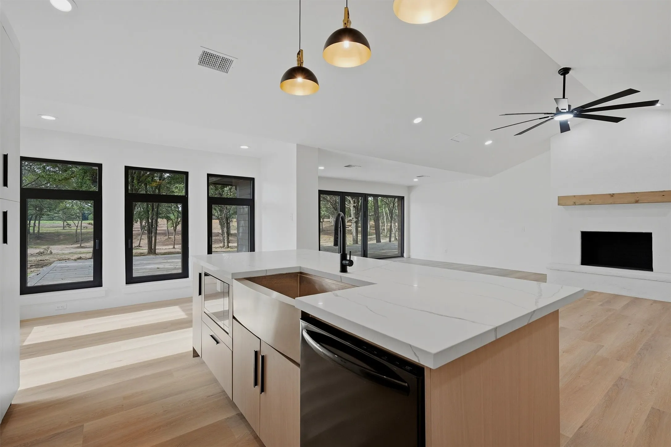 Open-concept living area featuring a kitchen island with a white countertop and undermount sink, a built-in dishwasher, and pendant lighting