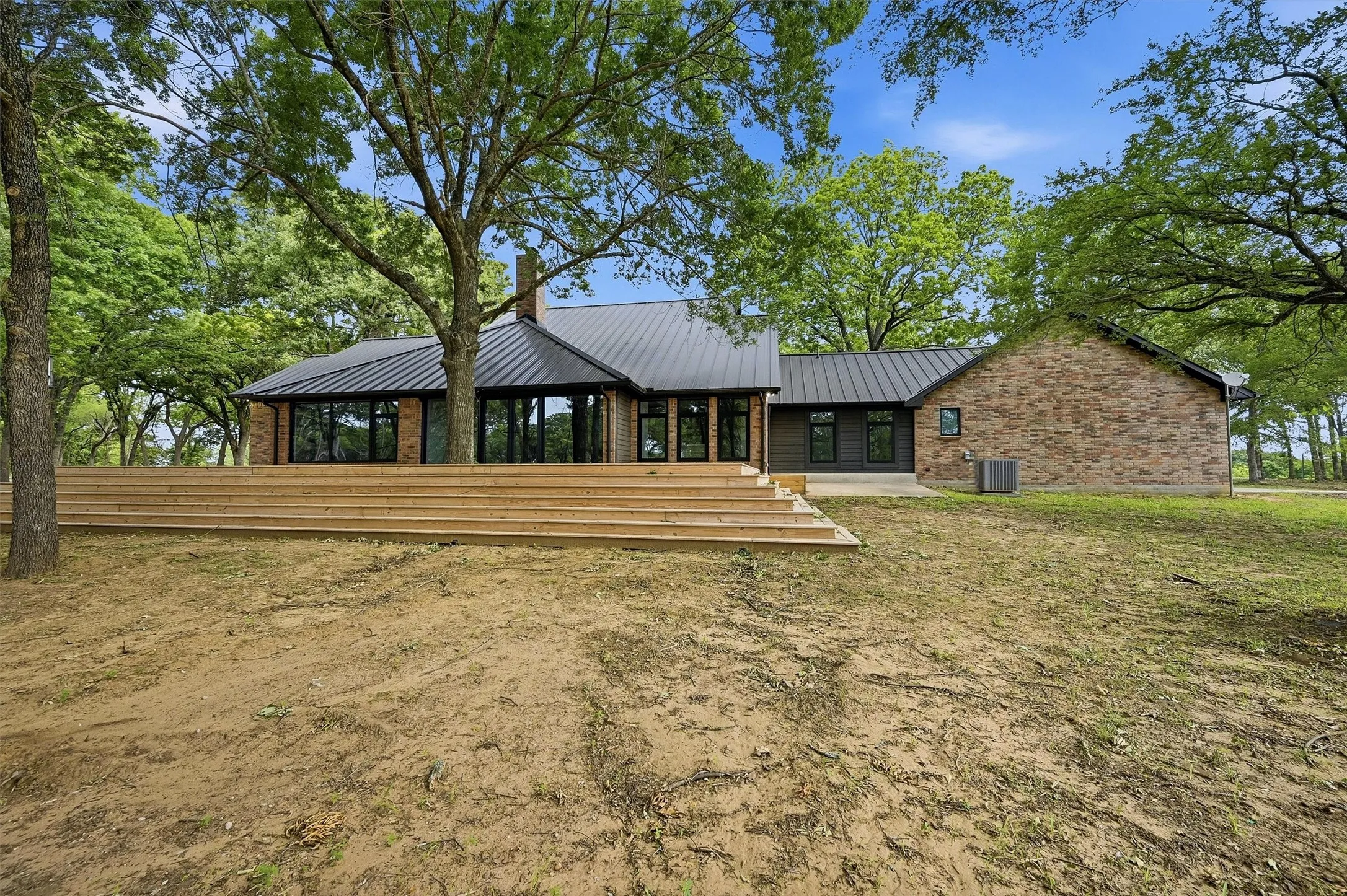 Contemporary residence featuring a black metal roof, brick and dark siding exterior, and extensive back decking