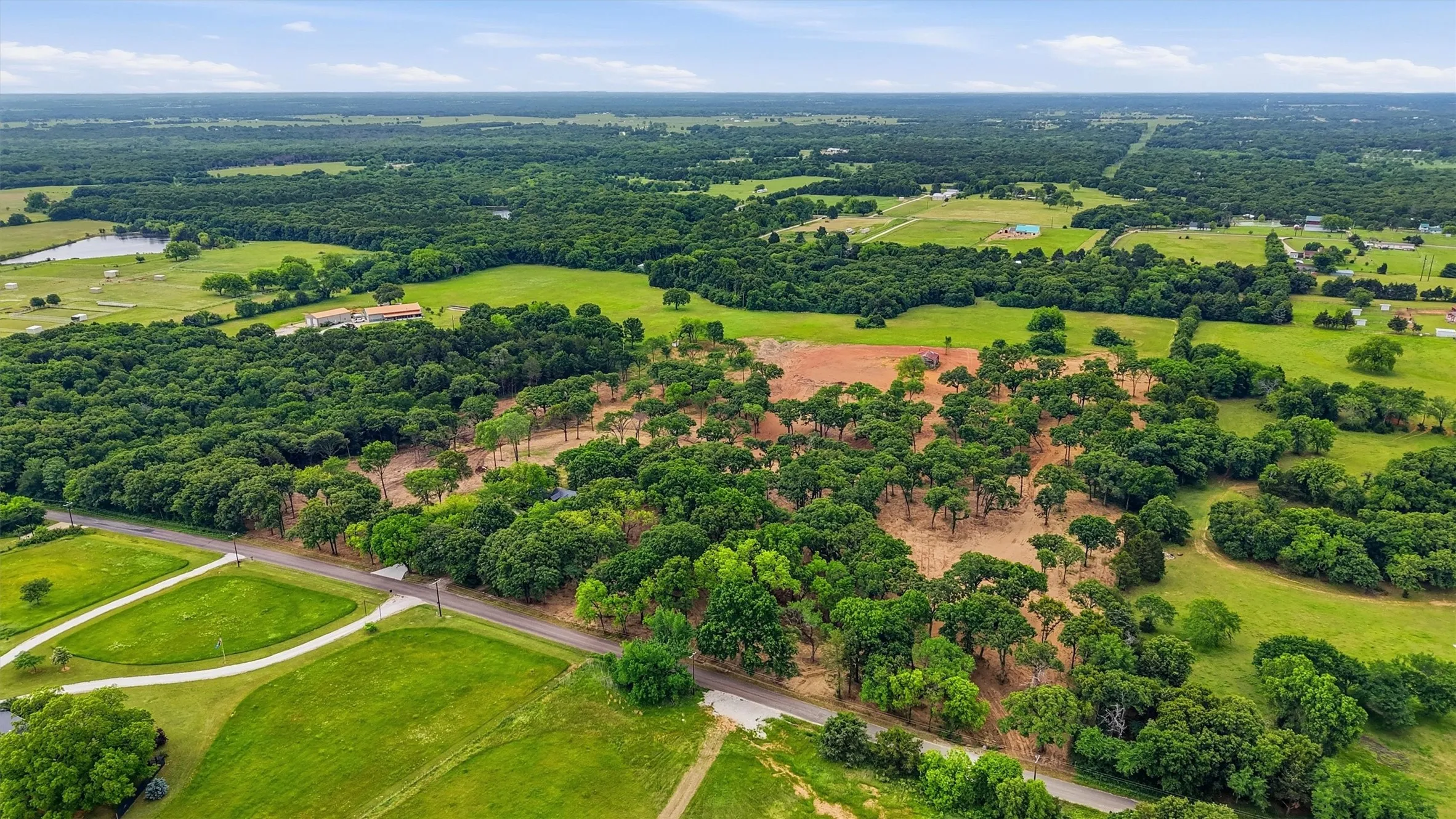 Expansive acreage featuring mature trees, open clearings, a paved road, and a distant pond