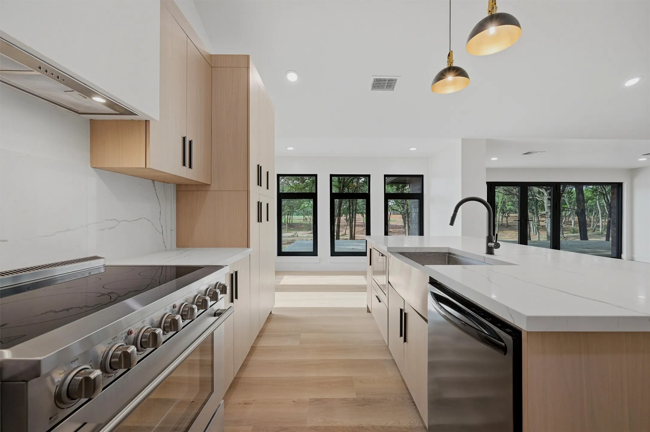 Modern kitchen featuring a stainless steel range with hood, light wood-finish cabinetry, a large kitchen island with a stainless steel farmhouse sink, and a black gooseneck faucet