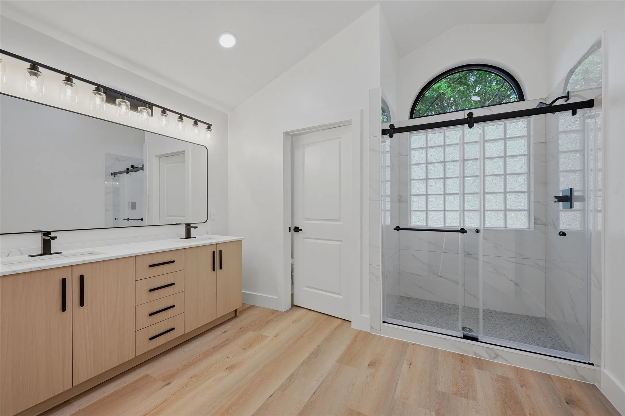 Spacious bathroom featuring a dual vanity with light wood-finish cabinetry, black hardware, and an expansive rectangular mirror