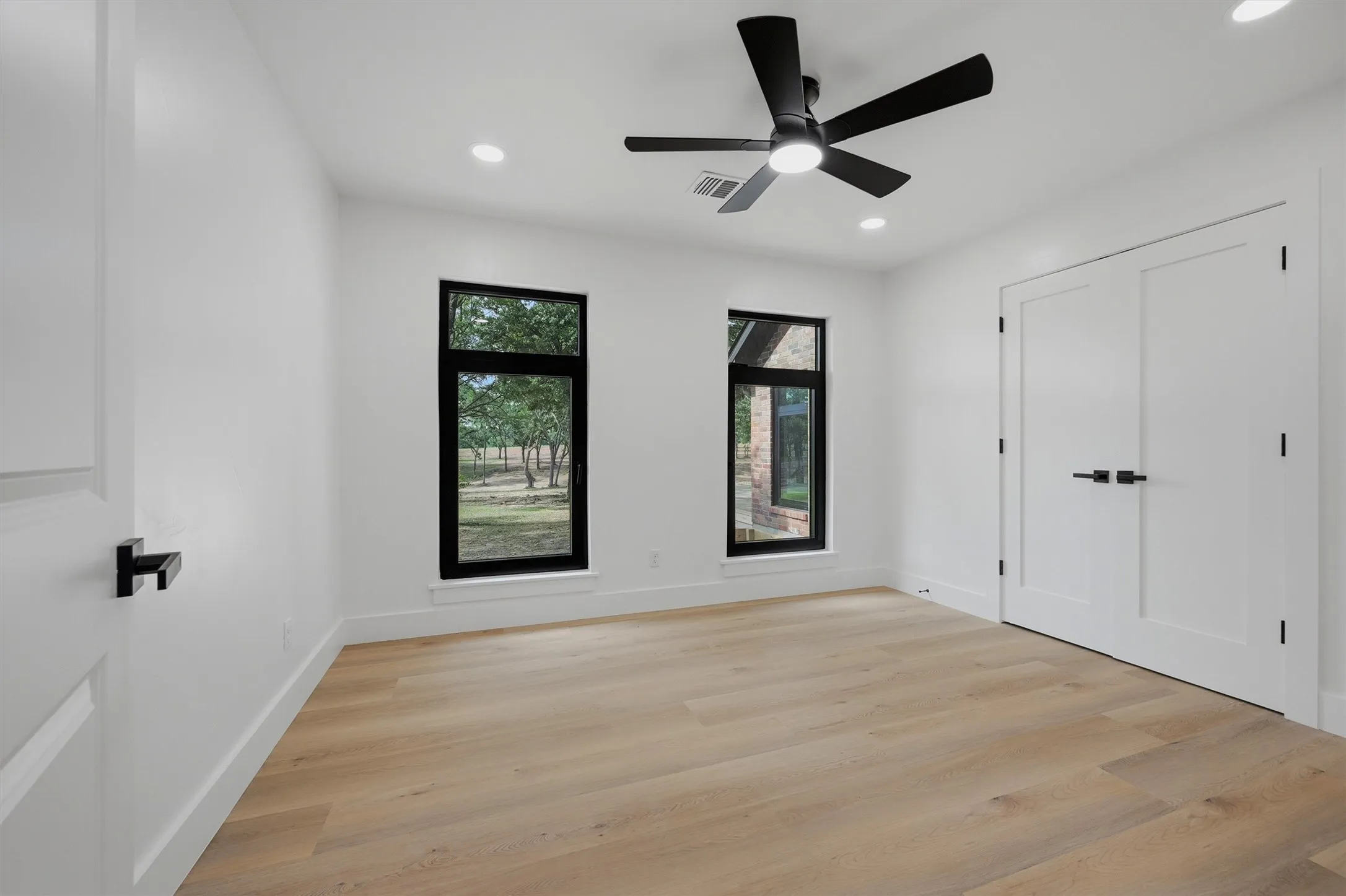 Bright room featuring wood-finish flooring, white walls, and a black ceiling fan with integrated lighting