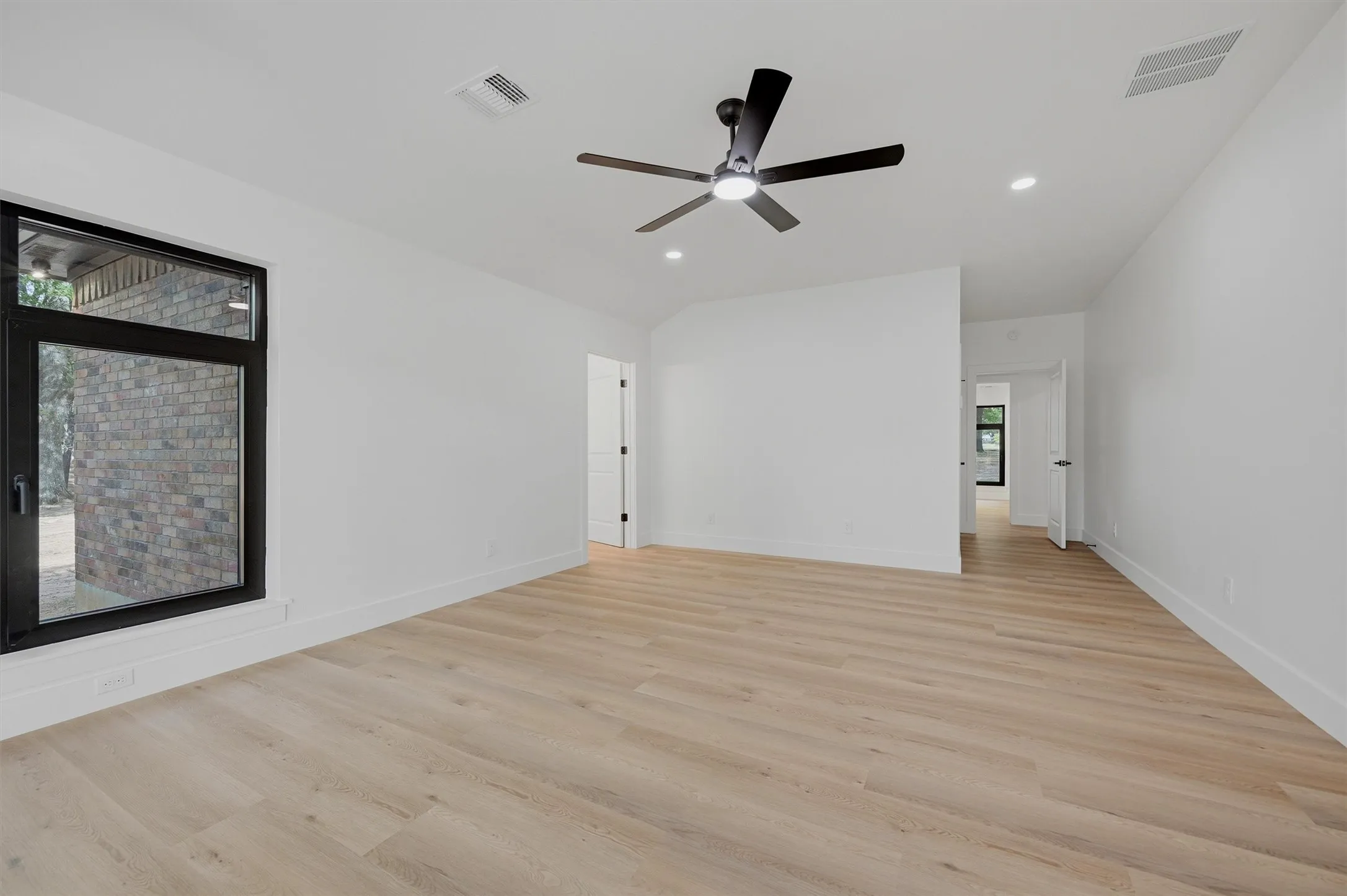 Spacious room featuring light wood-finish flooring, crisp white walls, and a contemporary ceiling fan with integrated lighting