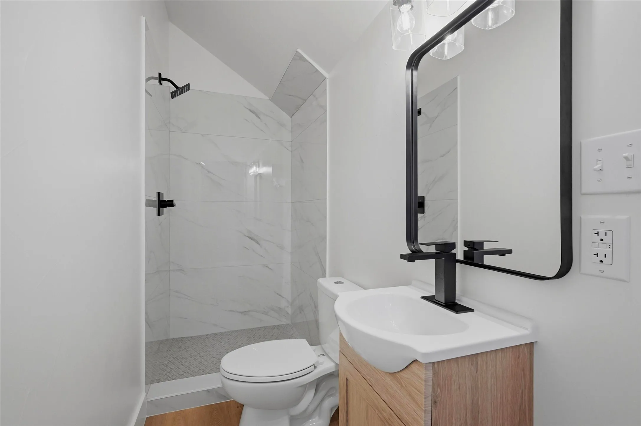 Bathroom featuring a walk-in shower with large format white tile, a dark-finish rainfall showerhead, and dark-finish fixtures