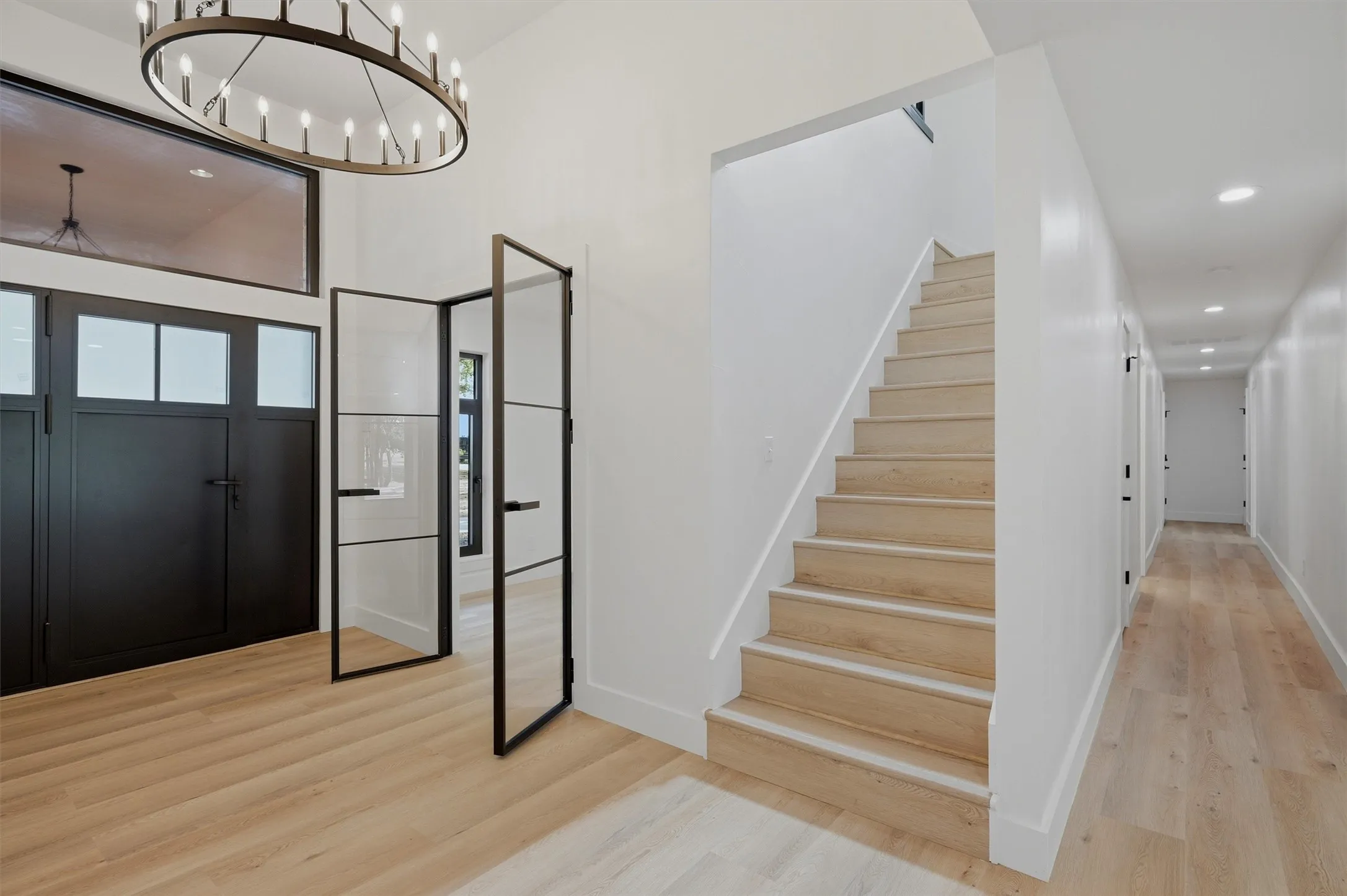 Entryway featuring a large chandelier, double black entry doors with upper window panels, and wood-finish flooring