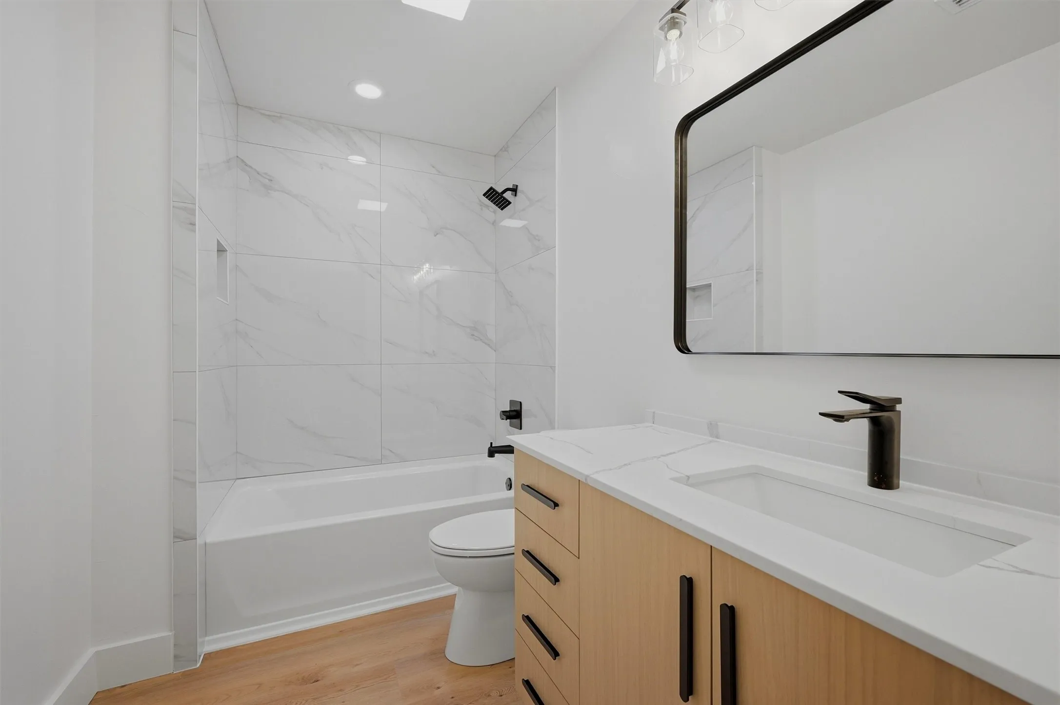 Modern bathroom featuring a contemporary vanity with a rectangular undermount sink, matte black fixtures, and wood-finish flooring