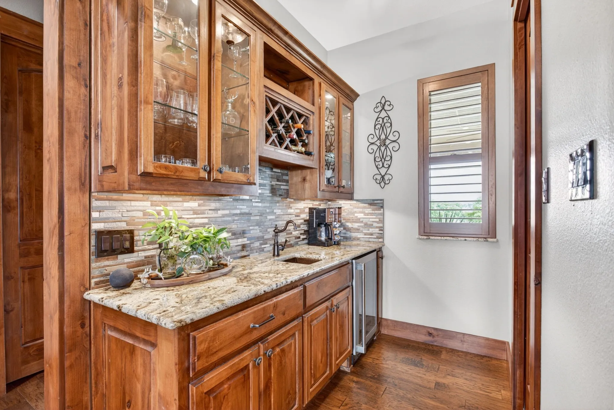 Built-in wet bar featuring custom wood cabinetry, granite countertops, a stone tile backsplash, and a wine rack