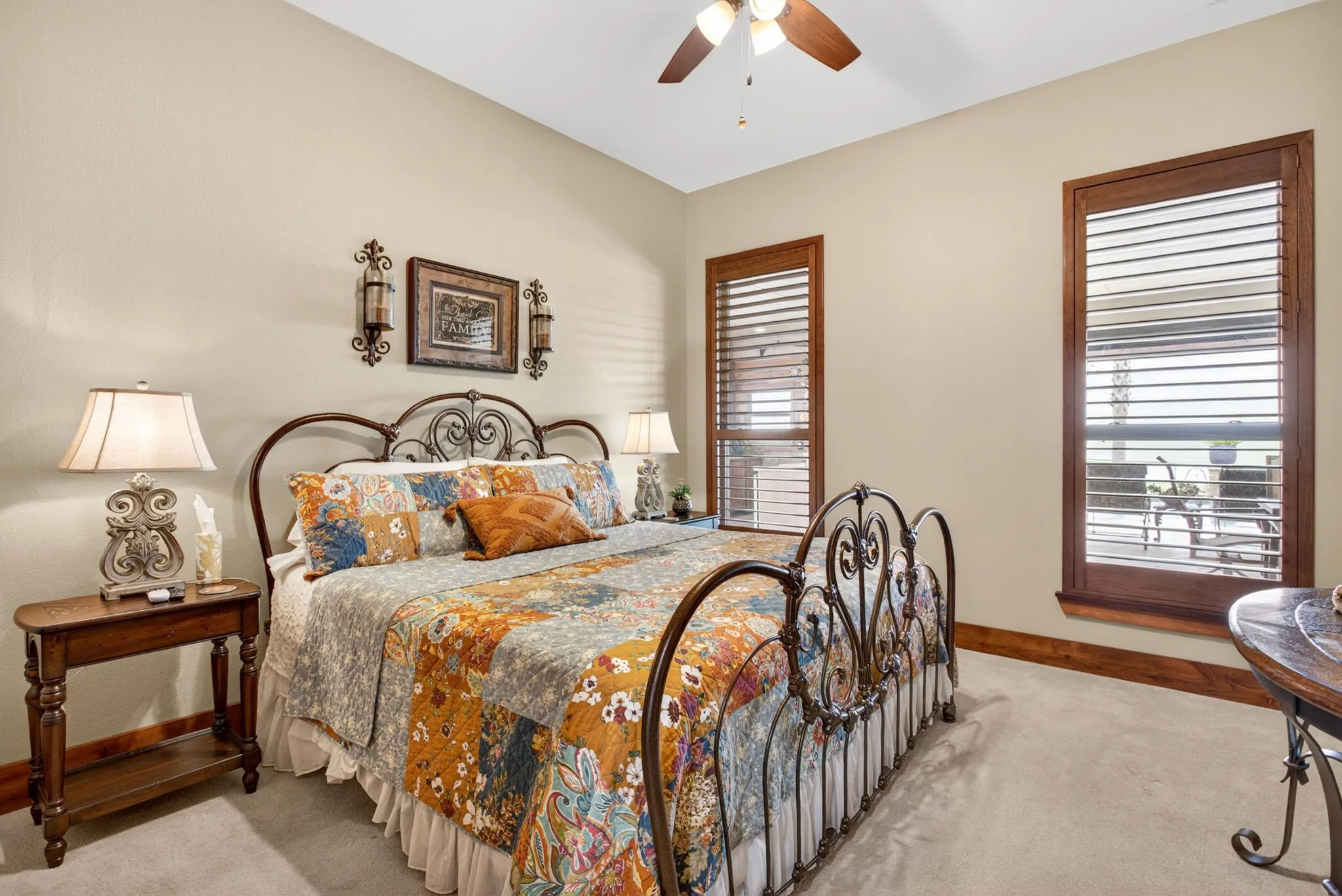 Carpeted room featuring two windows with wood plantation shutters, a ceiling fan, and decorative wall sconces