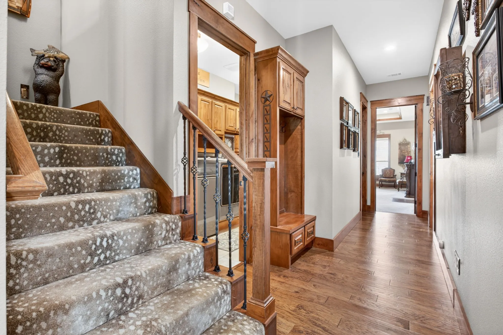 Foyer featuring wood-finish flooring, a built-in hall tree with storage, a staircase with patterned carpet and wrought iron balusters, and wood trim throughout