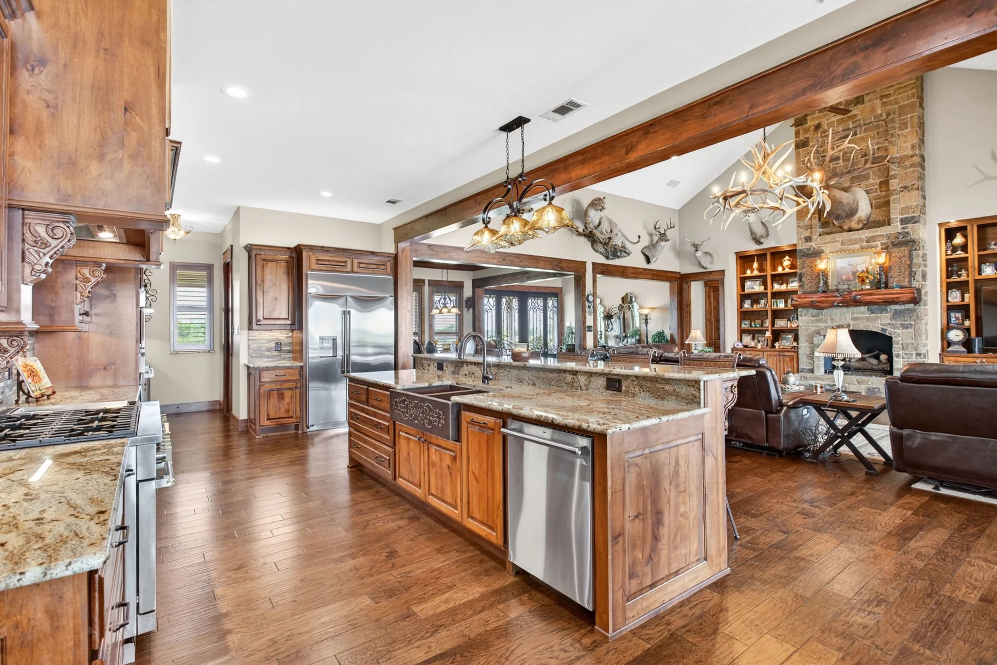 Open-concept kitchen featuring wood-finish flooring, granite countertops, custom cabinetry, stainless steel appliances, and an expansive center island with an apron-front sink