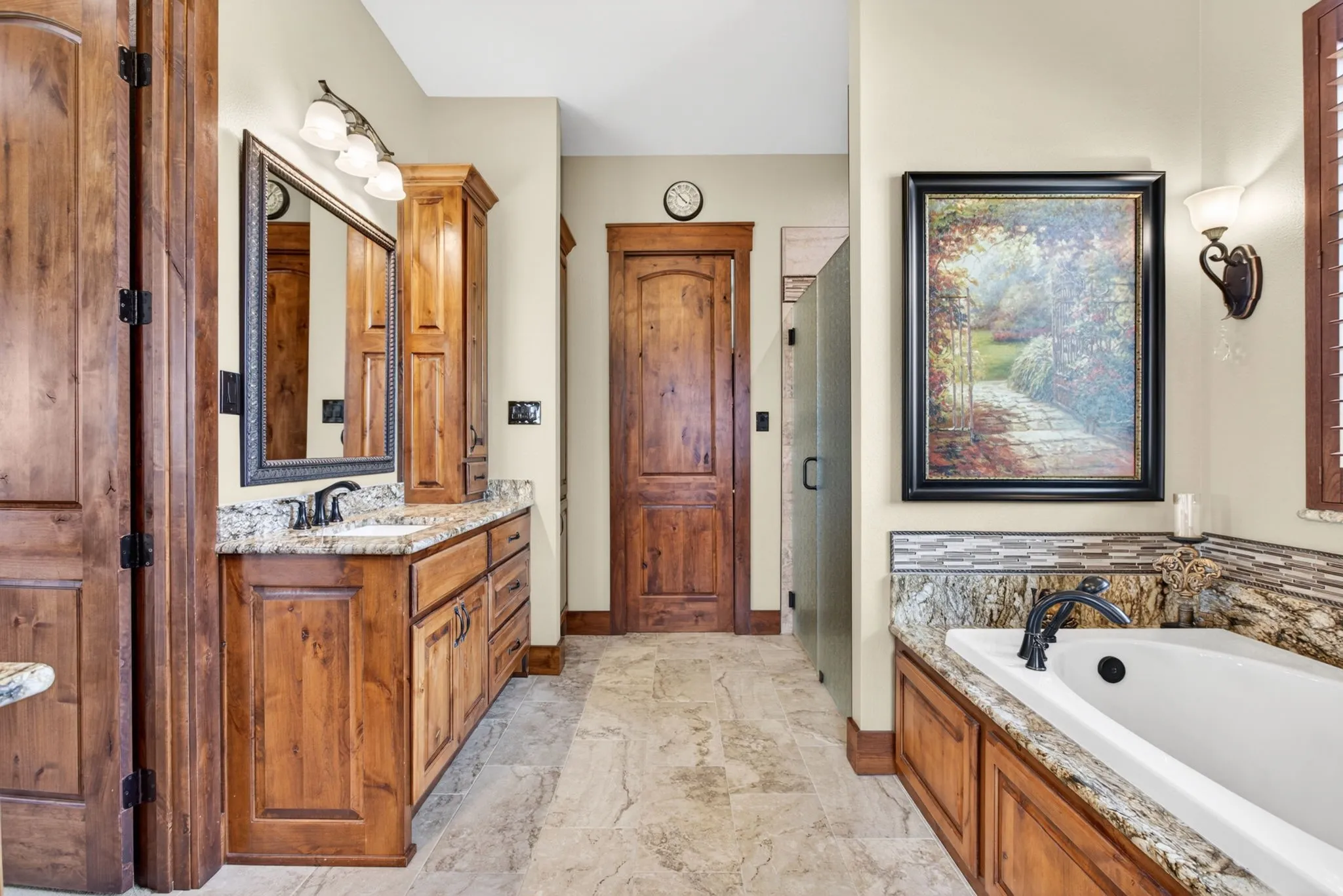 Spacious bathroom featuring a built-in soaking tub with a granite surround, a wood-finish vanity with a granite countertop and integrated sink, a large wall mirror, and tiled flooring