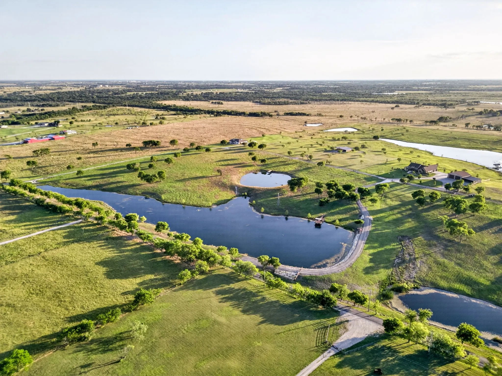 Expansive rural property featuring multiple ponds, scattered mature trees, winding roadways, and several structures