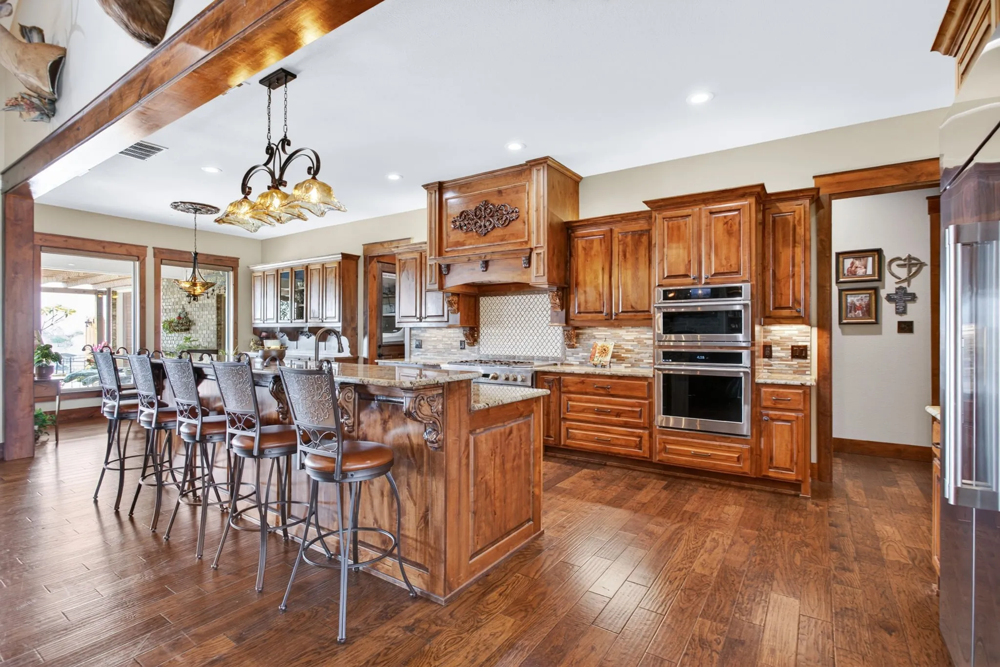 Gourmet kitchen featuring wood-finish flooring, custom wood cabinetry, a large kitchen island with seating, stainless steel double ovens, and a tile backsplash