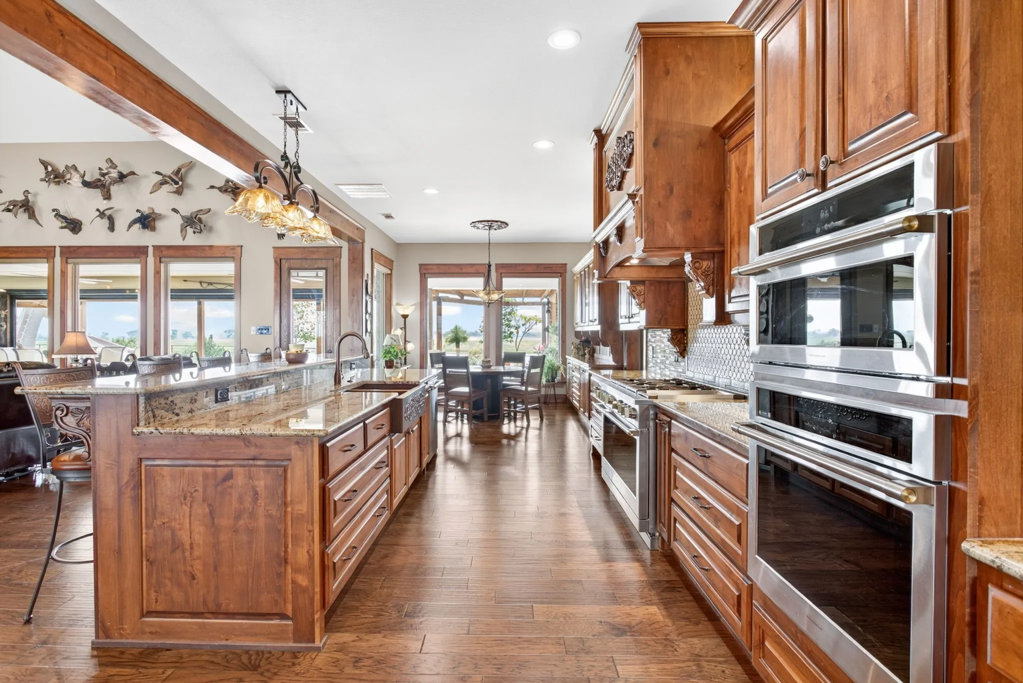 Gourmet kitchen featuring custom wood cabinetry, granite countertops, wood-finish flooring, a double wall oven, and a tiled backsplash