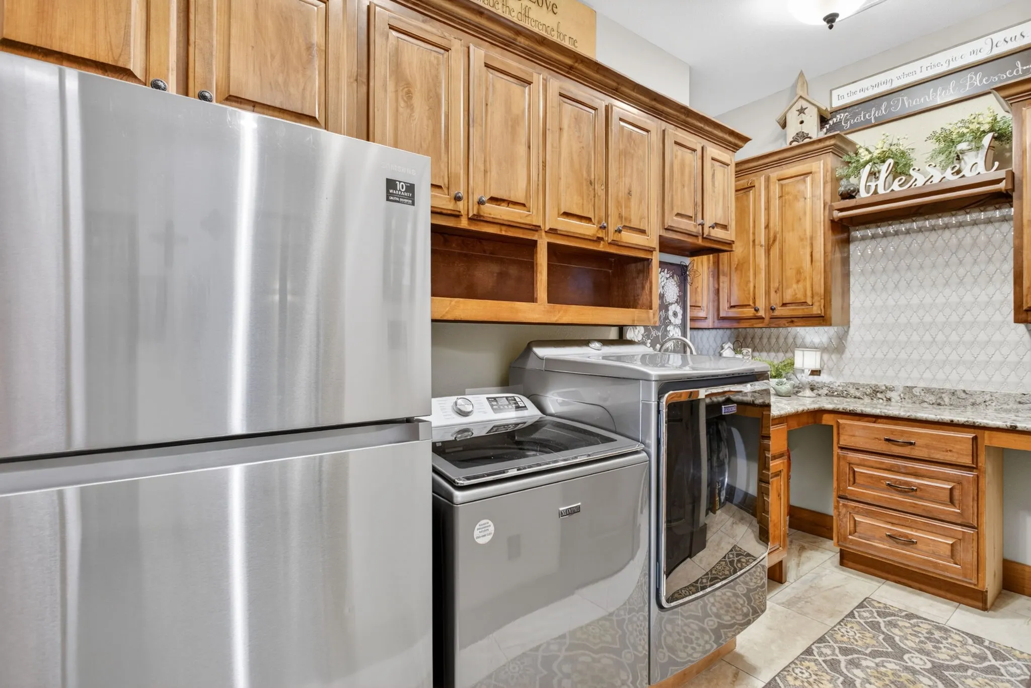 Laundry area featuring custom wood cabinetry, granite-style countertops, a decorative tile backsplash, and tile flooring