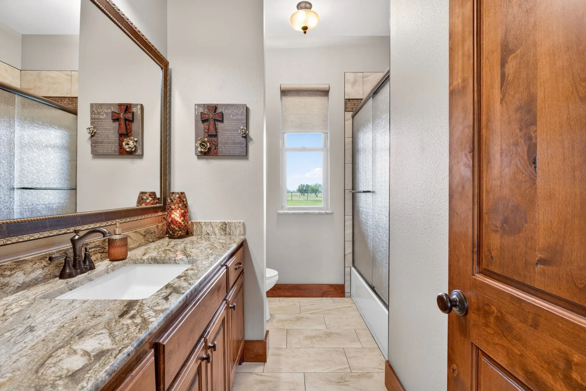 Bathroom featuring a wood-finish vanity with an undermount sink, a patterned stone countertop, and an ornate framed mirror