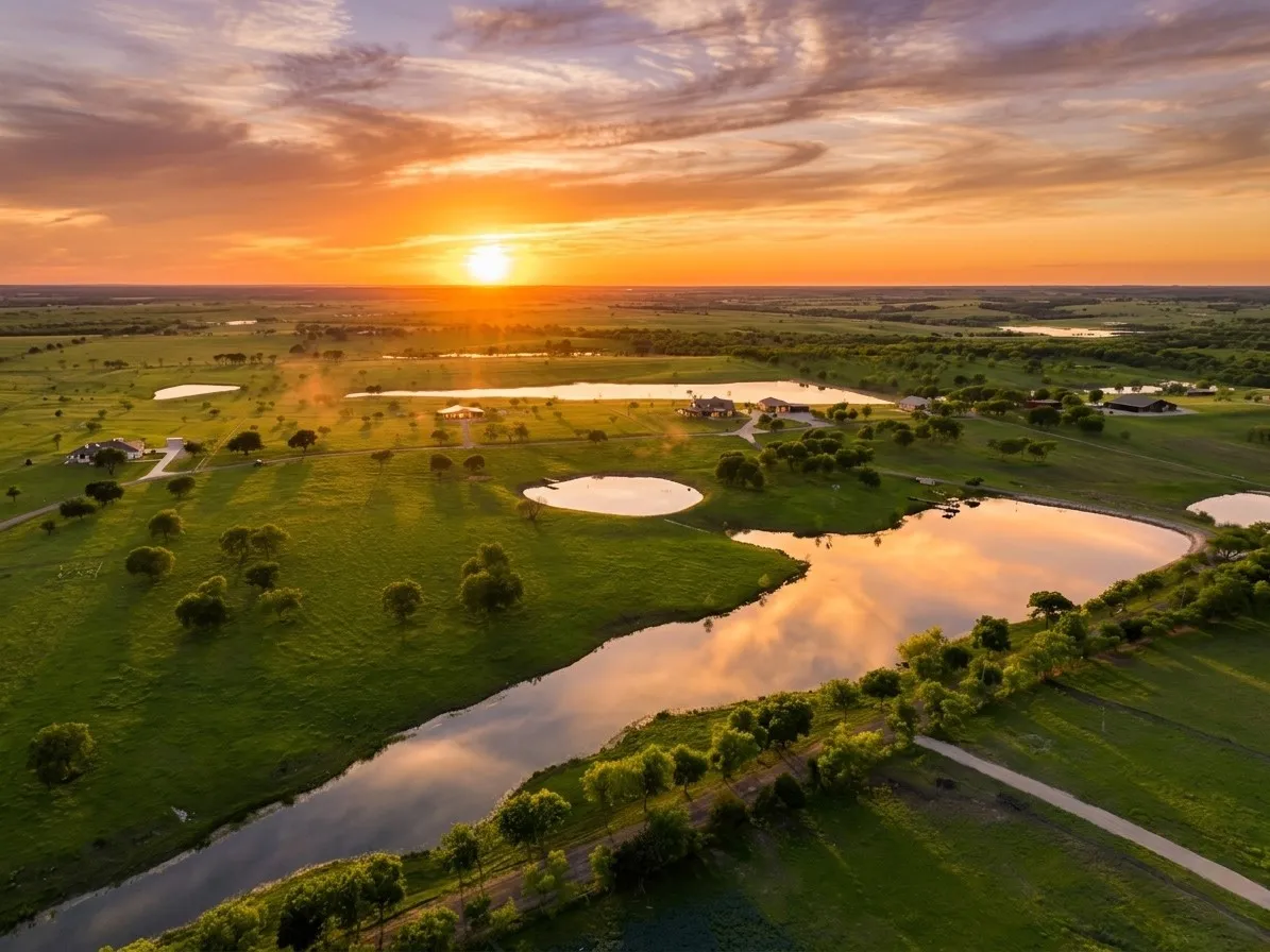 Expansive property featuring multiple bodies of water, extensive green acreage, scattered mature trees, and several residential structures
