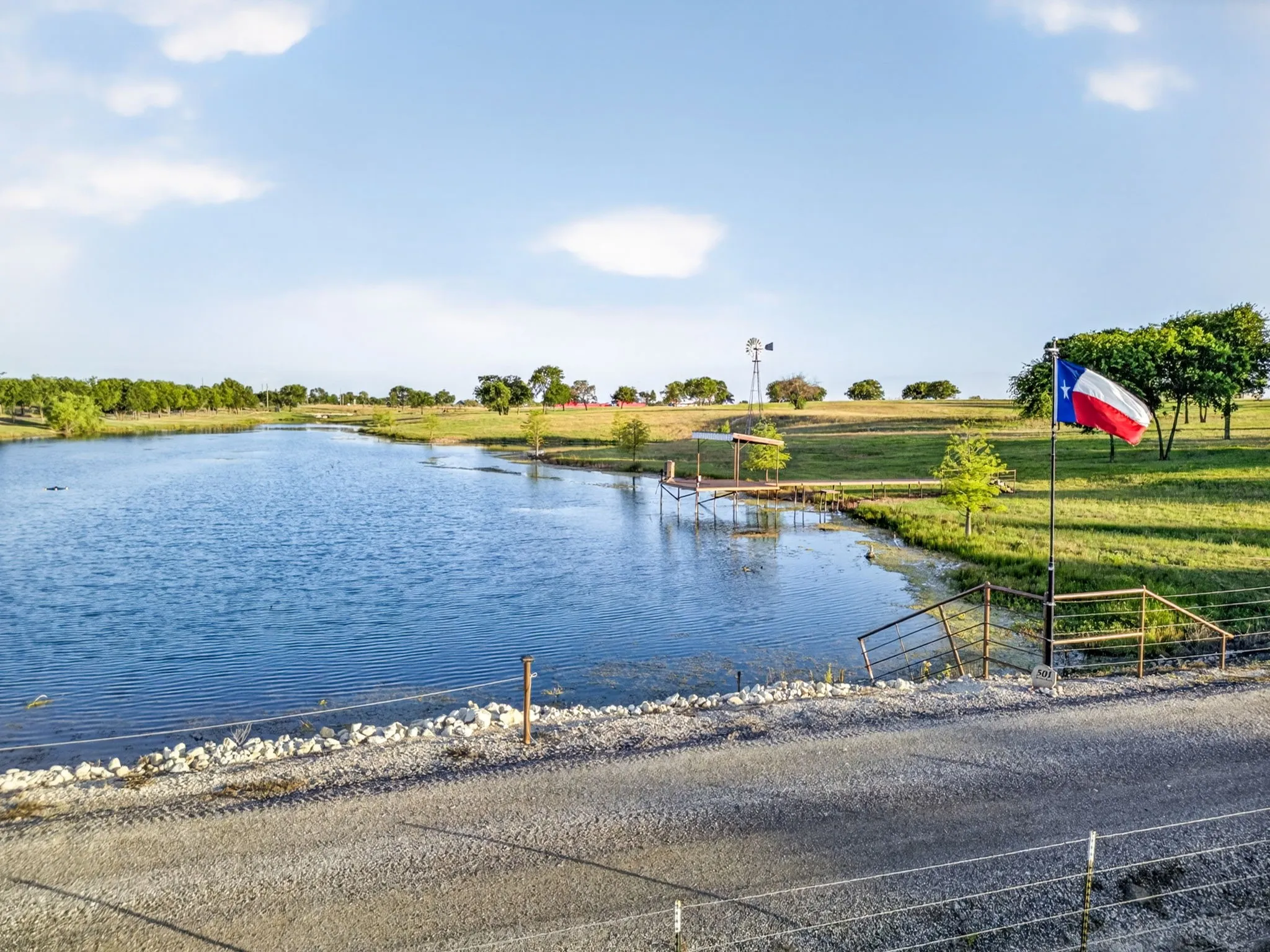 Expansive pond frontage with a gravel bank and surrounding green fields