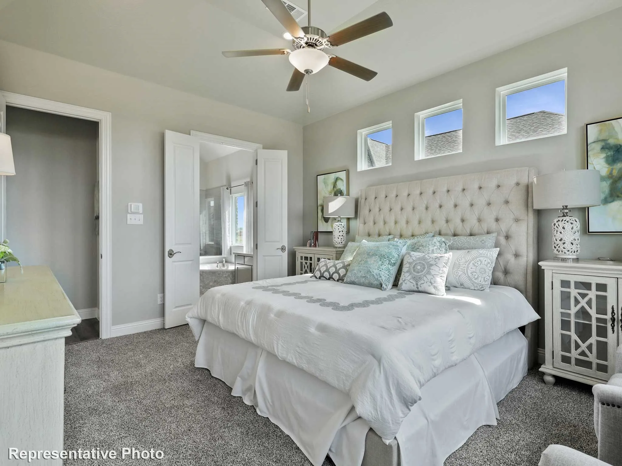 Carpeted bedroom featuring a ceiling fan with integrated lighting, three transom windows, and double doors opening to a bathroom with a soaking tub
