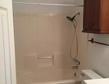 Bathtub with an integrated shower, white tile surround, and a handheld shower fixture