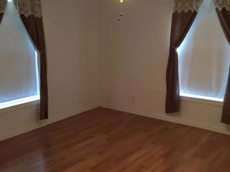 Spacious interior room featuring wood-finish flooring, white baseboards, and two windows