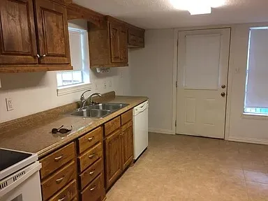 Kitchen featuring wood cabinetry, laminate countertops, a double basin stainless steel sink, tile flooring, and a built-in dishwasher