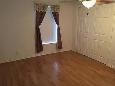 Room featuring wood-finish flooring, white walls, and a window with blinds