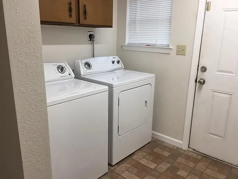 Laundry area featuring wood-finish cabinetry with dark hardware, a window with horizontal blinds, and a white paneled door