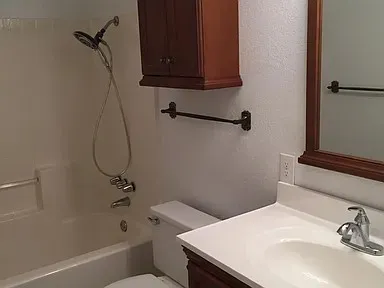 Bathroom featuring a white tub with an attached shower head, a white toilet, and a vanity with a white countertop and integrated sink