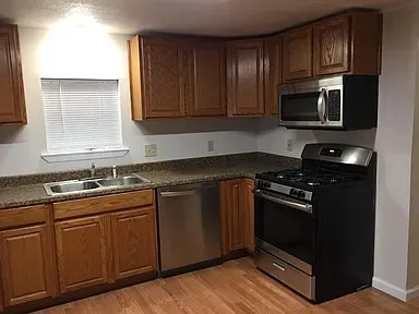 U-shaped kitchen featuring light wood cabinetry with brushed nickel hardware, laminate countertops, a stainless steel double basin sink, and wood-finish flooring