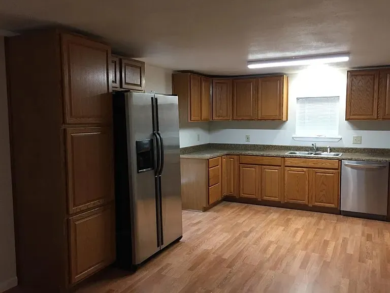 Kitchen featuring wood-finish flooring, oak cabinetry, granite-patterned countertops, and a stainless steel dishwasher
