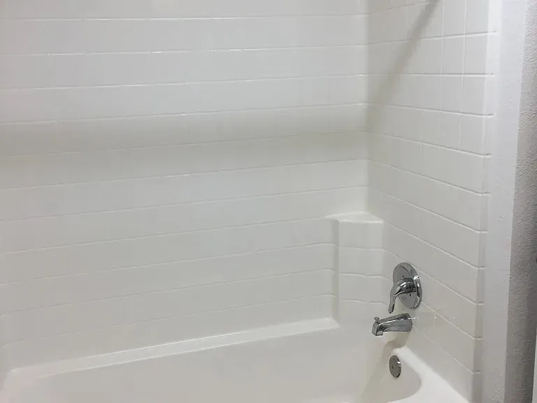 White bathtub with integrated shower, chrome fixtures, and white horizontal tile-patterned surround