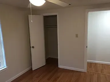Room with wood-finish flooring, ceiling fan with integrated lighting, and white baseboards