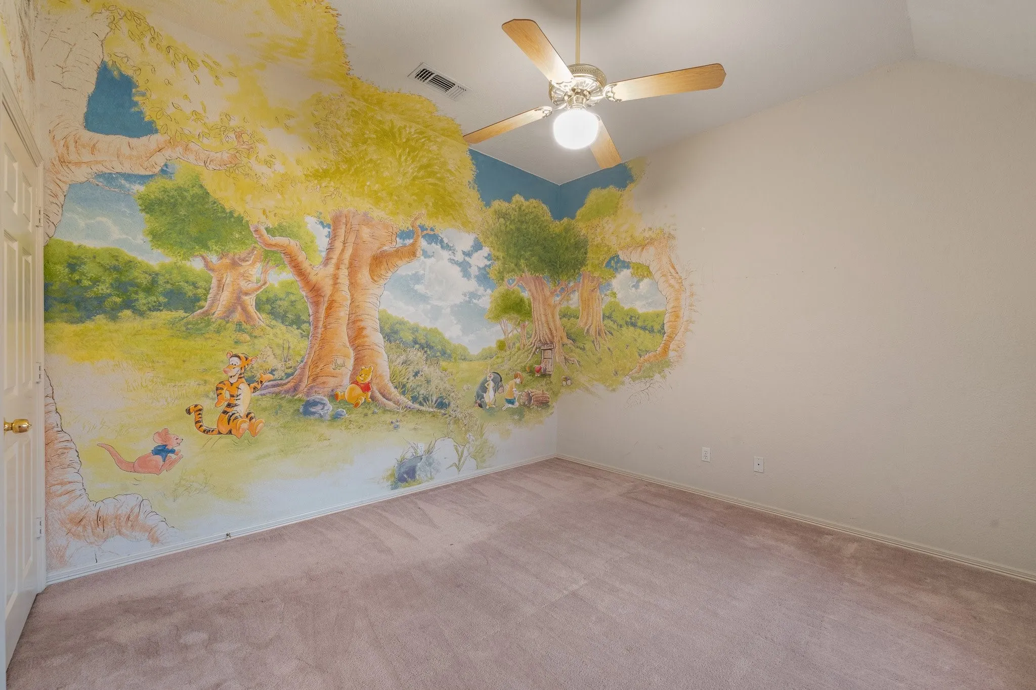 Vaulted ceiling room with an artistic mural, ceiling fan with wood-finish blades, light-toned carpeting, and a six-panel door with brass hardware