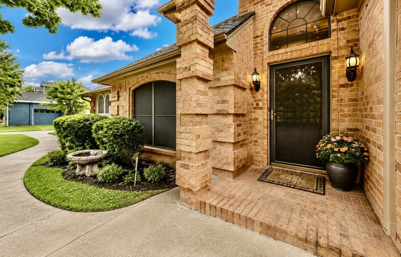 Brick exterior featuring an arched transom window, a black screen door, and matching sconce lighting