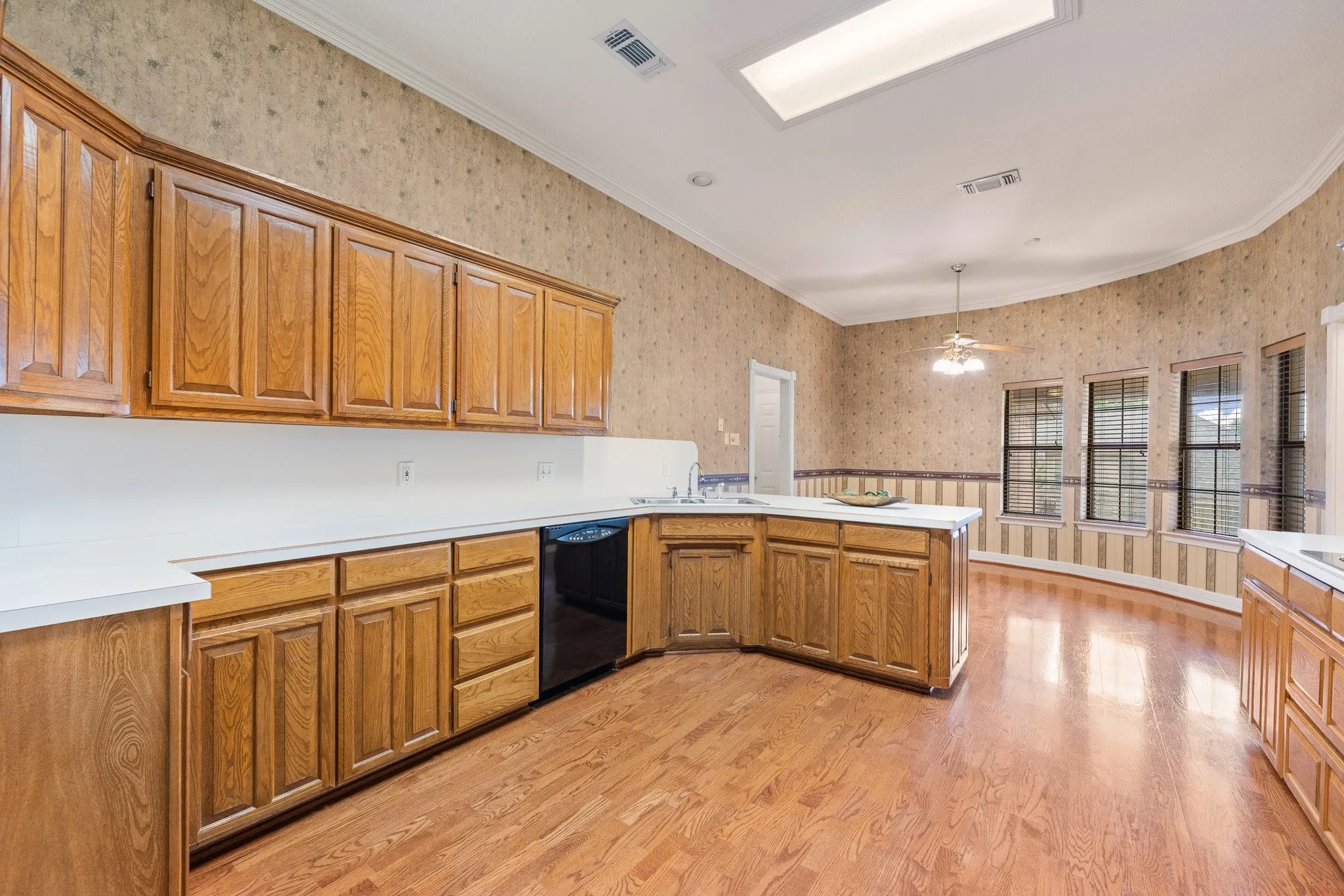 Kitchen featuring extensive wood cabinetry, white countertops, built-in dishwasher, wood-finish flooring, and multiple windows