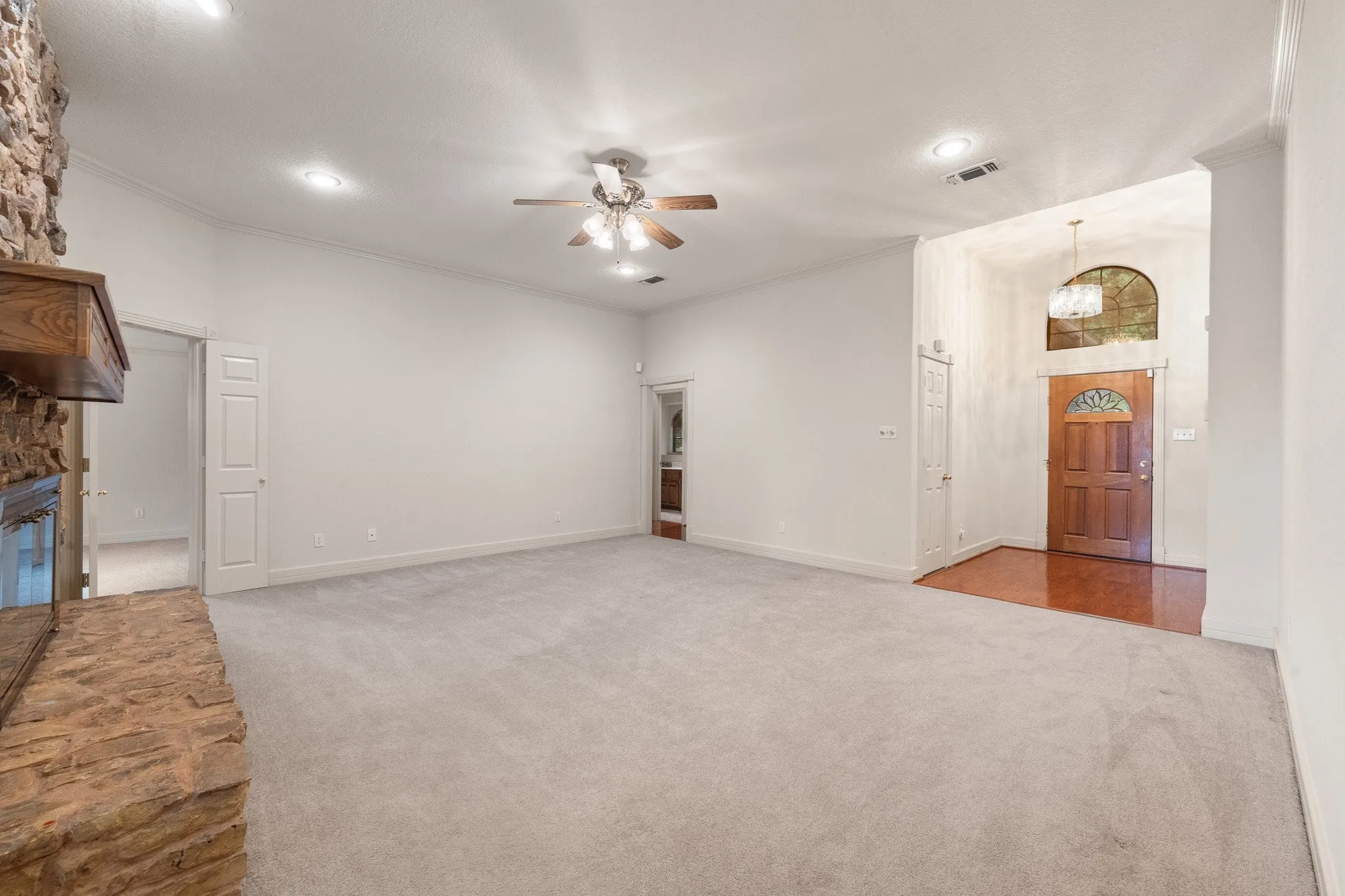 Spacious living area featuring light-toned carpeting, a stone fireplace, and a wood mantel