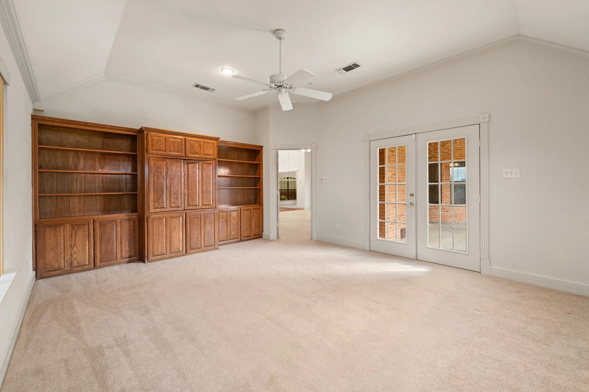 Spacious room featuring vaulted ceilings, a ceiling fan, and extensive built-in wooden cabinetry and shelving