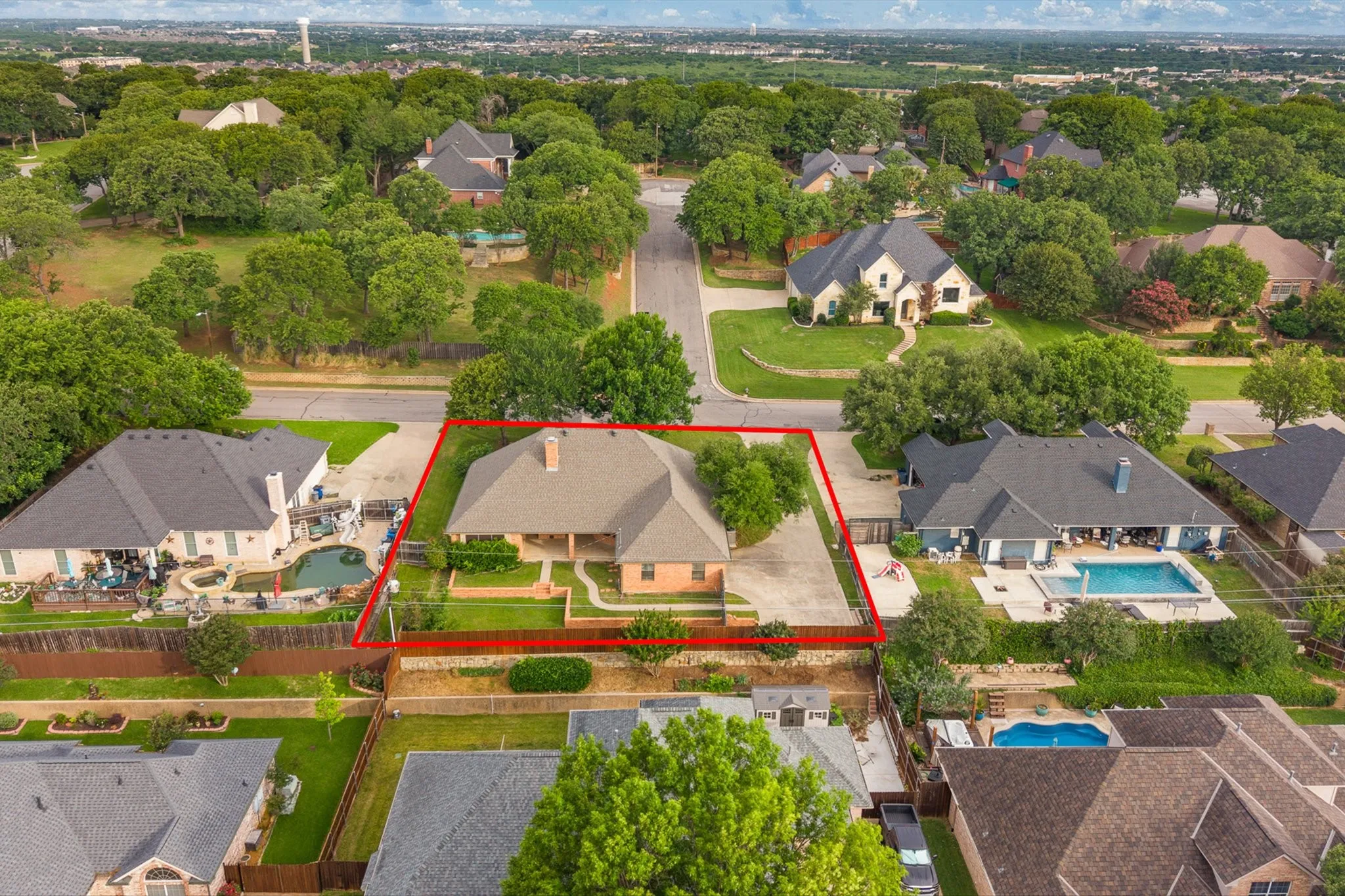 Traditional brick residence with a gabled roof, featuring an attached front porch, mature landscaping, and an expansive concrete driveway