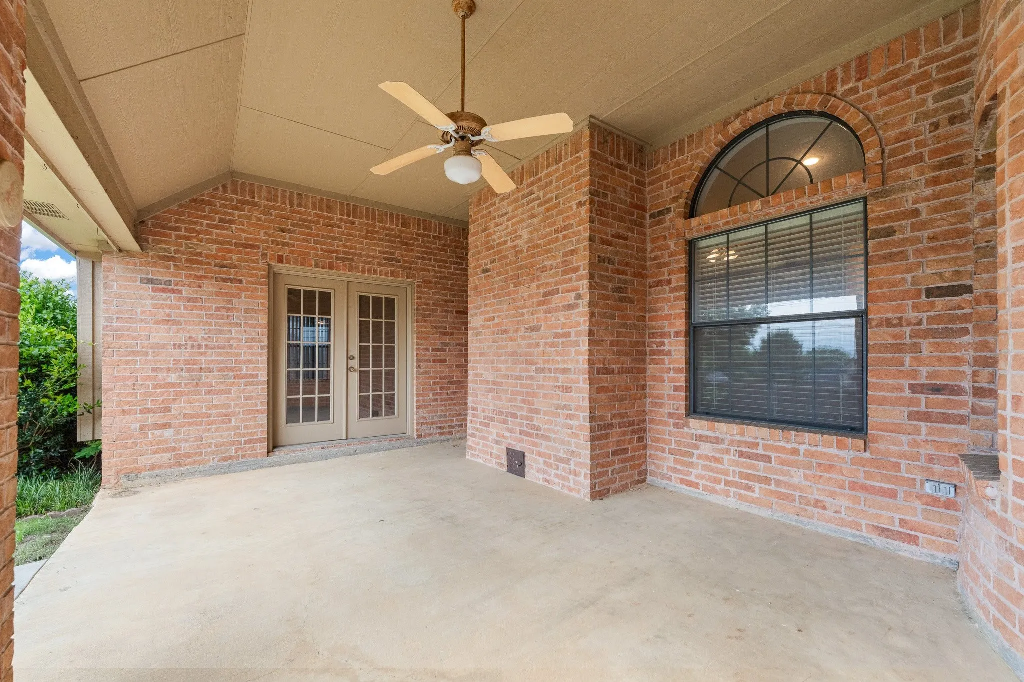Covered patio featuring brick construction, a ceiling fan, concrete flooring, and French doors
