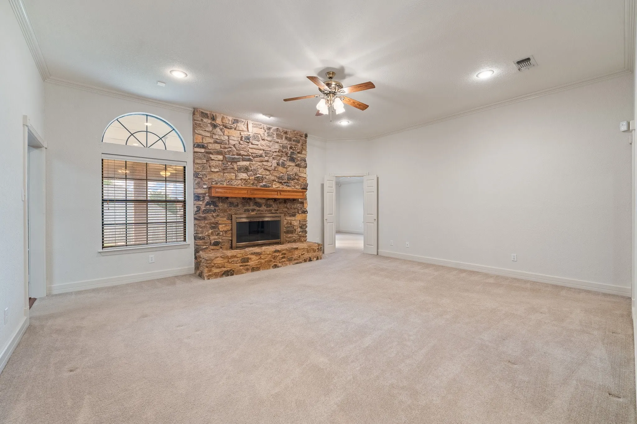 Spacious room featuring a stone-clad fireplace with a wood mantel, a large window with an arched transom, recessed lighting, and a ceiling fan